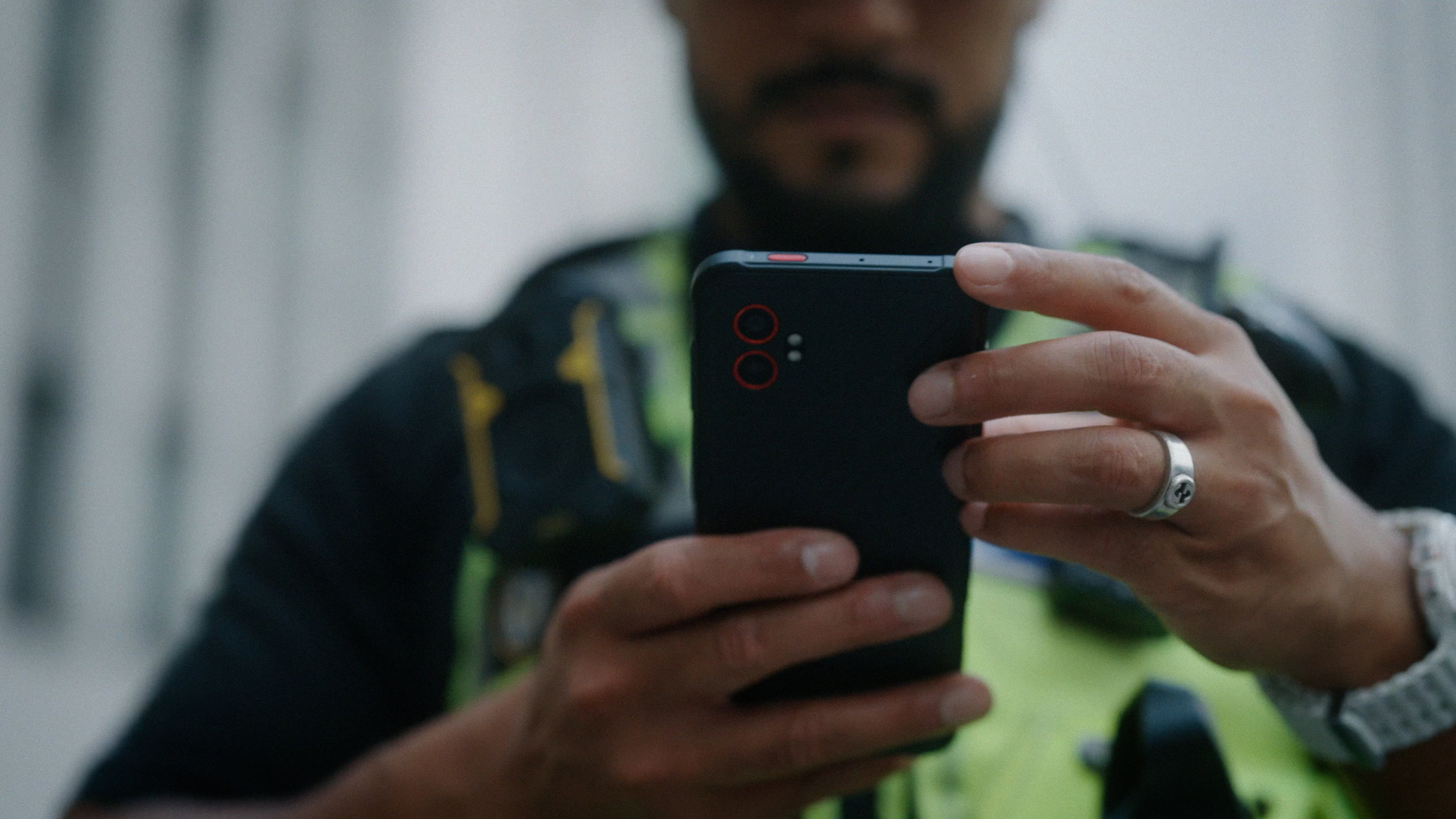 A police officer in uniform holding a smartphone while using it outdoors.